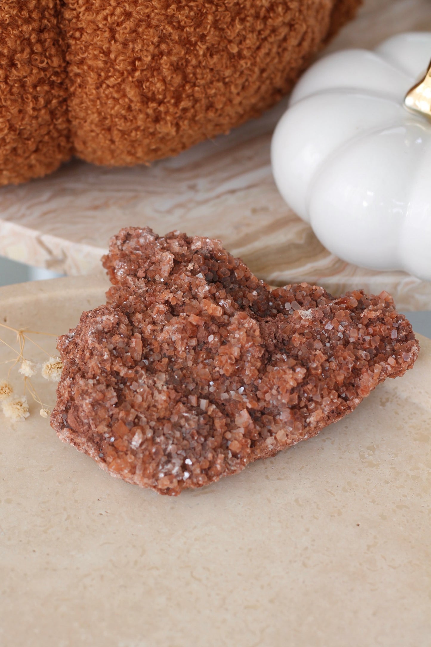 Een bruine Aragoniet kristalcluster geplaatst op een lichtgekleurde ondergrond. De Aragoniet heeft een ruwe, kristallijne textuur met talrijke kleine, fonkelende facetten.