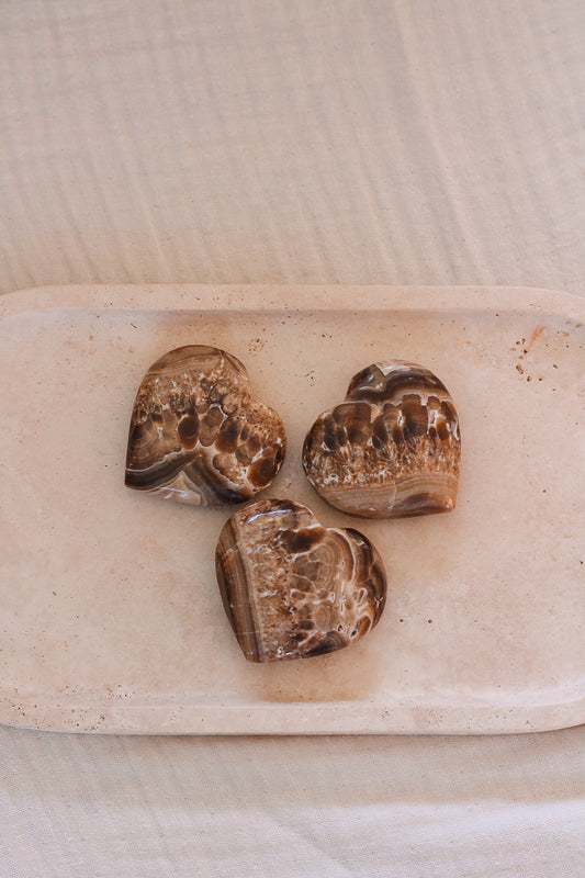 Drie handgeslepen aragoniet hartjes in zachte beige en bruine tinten, symbool voor aardende energie en emotionele balans