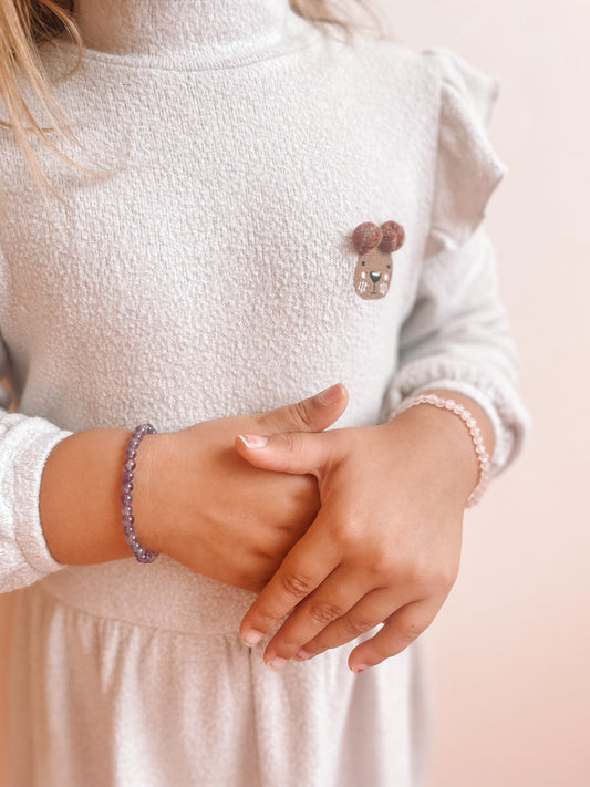 Abeelding van een kindje dat 2 soorten edelsteen armbandjes draagt rond haar polsen.