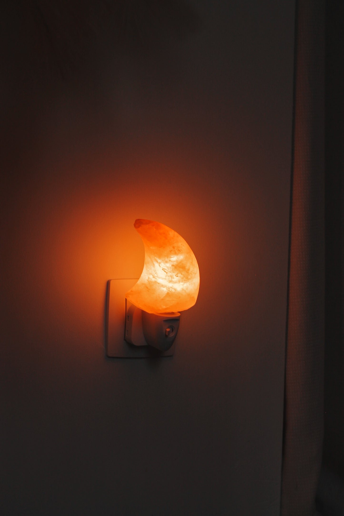 Een Himalaya zoutsteen nachtlamp in de vorm van een halve maan, brandend in het stopcontact.