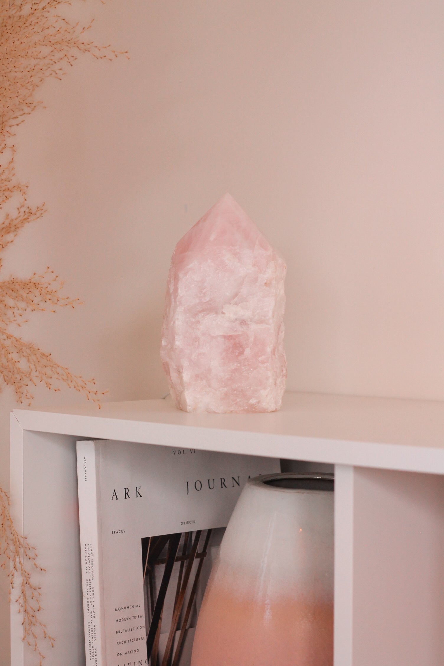 Rozenkwarts punt lamp op een witte kast waarin een boek en grote vaas met witte en roze kleuren staat. De lamp brand niet.