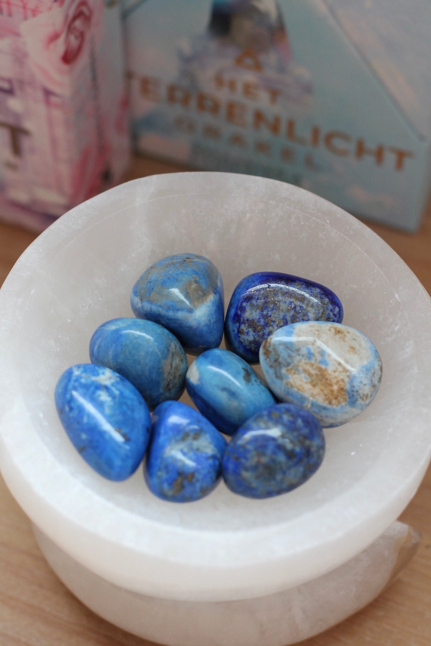 Een witte schaal met meerdere gepolijste Lapis Lazuli Tumble stenen. De stenen zijn blauw met enkele witte en gouden vlekjes.