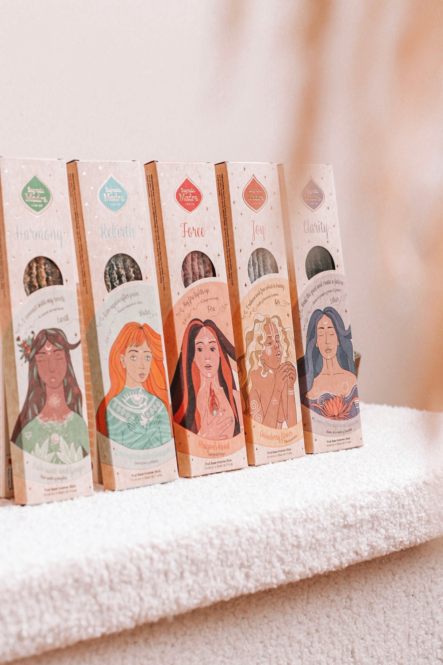 Vijf verpakkingen van producten, elk met een unieke illustratie van een vrouw op de voorkant. De verpakkingen staan in een rij. Elke verpakking heeft verschillende kleuren en ontwerpen, wat aangeeft dat het verschillende varianten zijn.