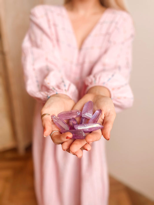 Een persoon in een lichtroze jurk met lange mouwen houdt meerdere Purple Aura puntjes in beide handen. De kristallen zijn doorschijnend en puntig aan één kant.