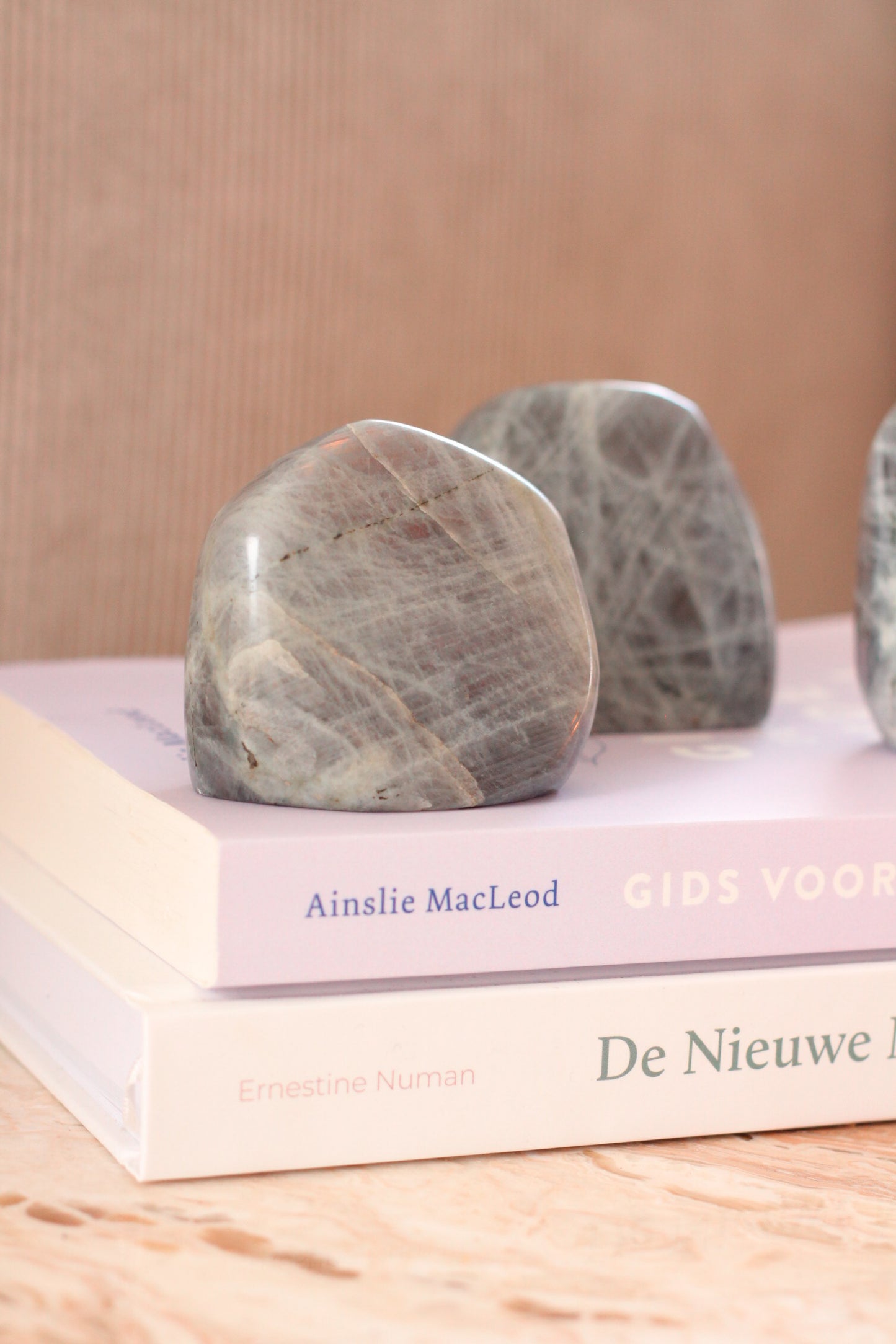 2 gepolijste roze labradoriet stenen liggen op twee gestapelde boeken, één van de stenen is gedetailleerd en de andere staat wazig in de achtergrond.