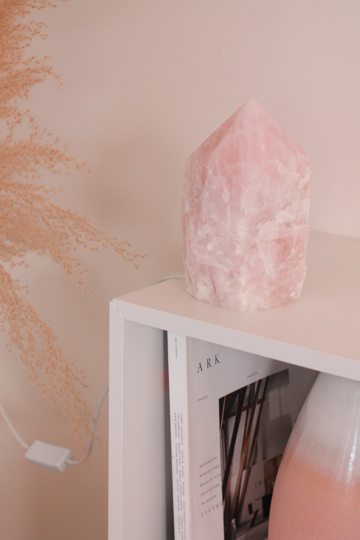 Rozenkwarts punt lamp, op een witte kast waarin een boek en grote vaas met witte en roze kleuren staat.
