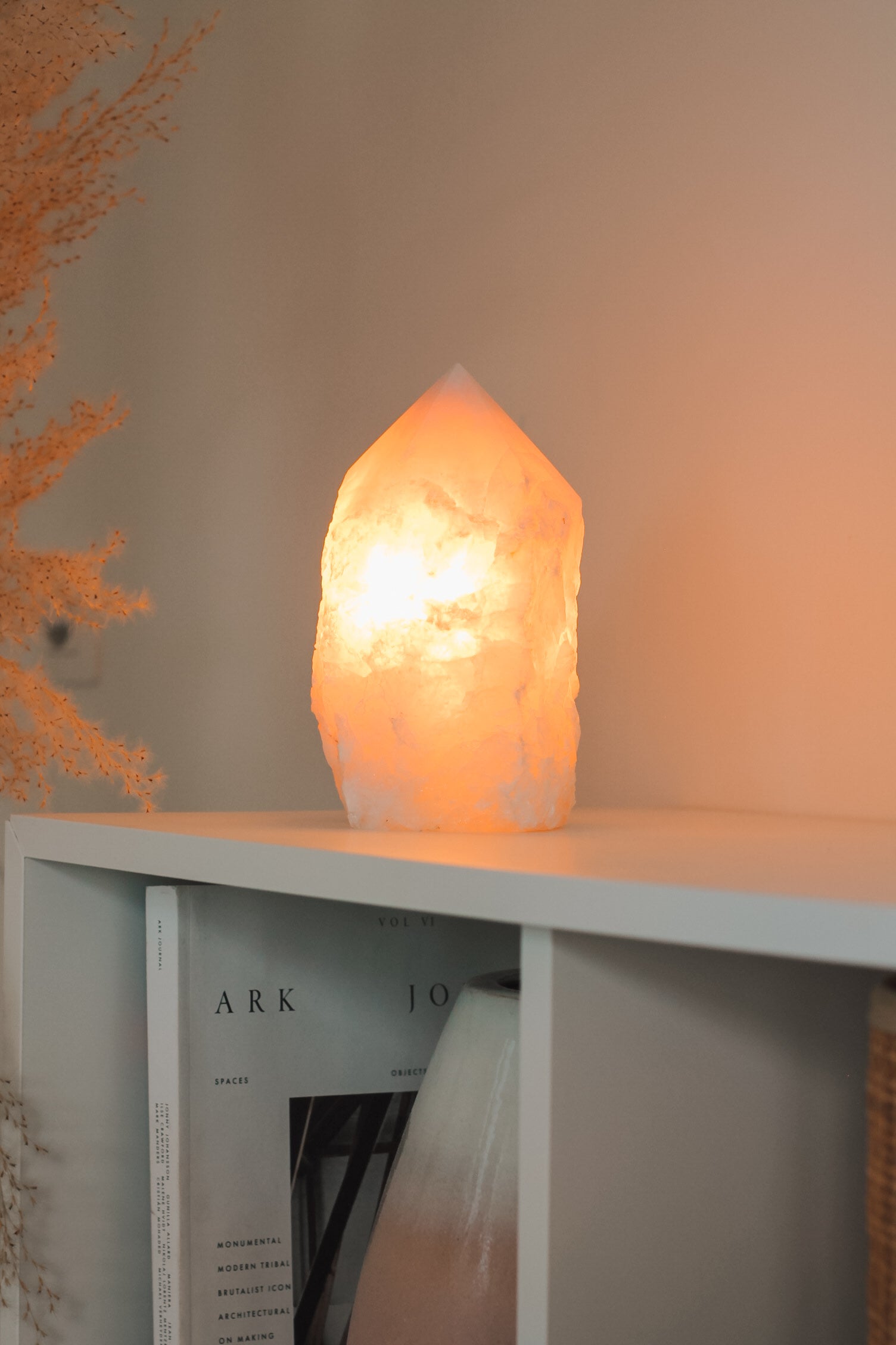 Rozenkwarts punt lamp, brandend op een witte kast waarin een boek en grote vaas met witte en roze kleuren staat. De lamp geeft een warme gloed.