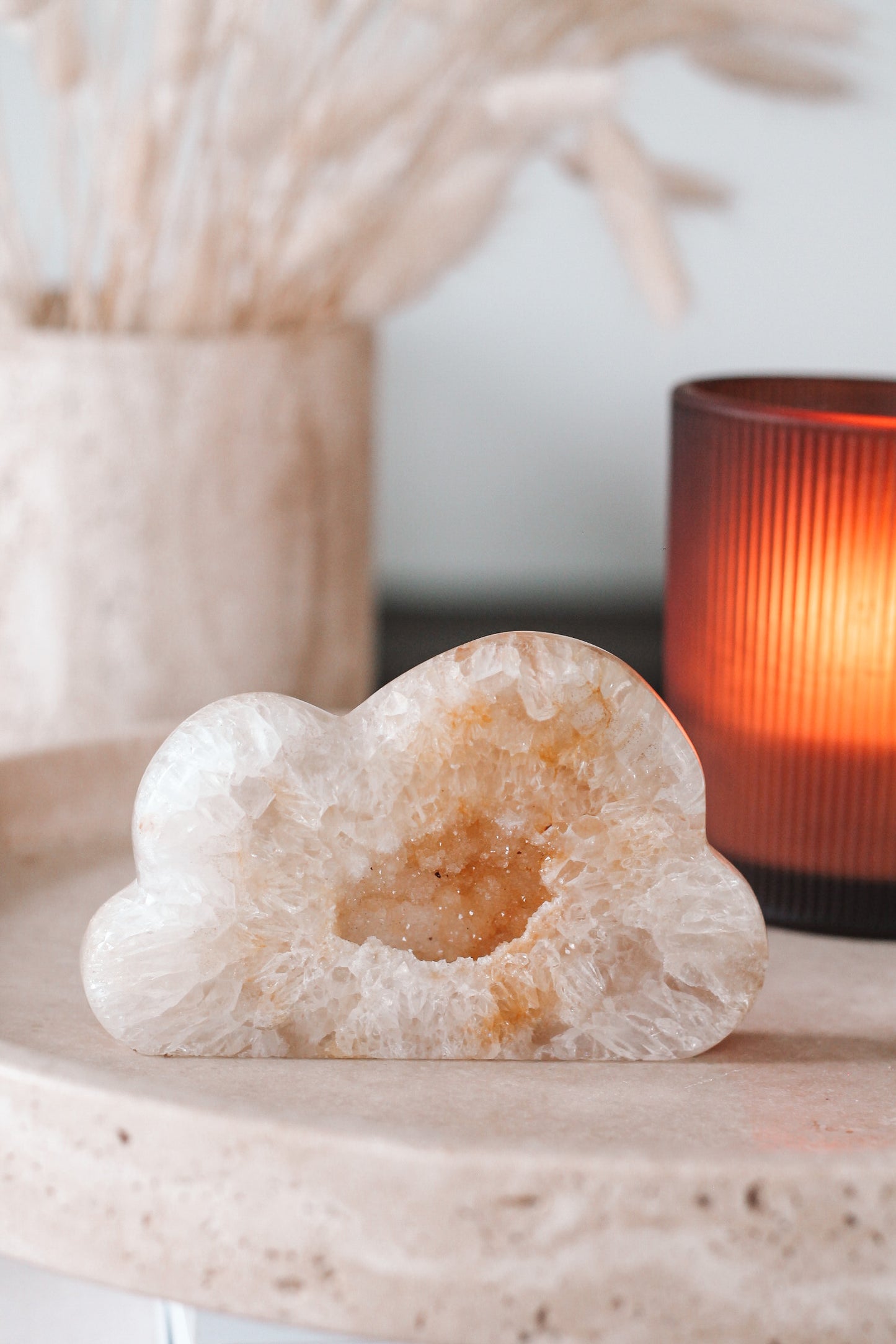 Een wolkvormig Agaat met een holle kern, geplaatst op een stenen oppervlak. Op de achtergrond staat een oranje kaars met een geribbelde textuur.