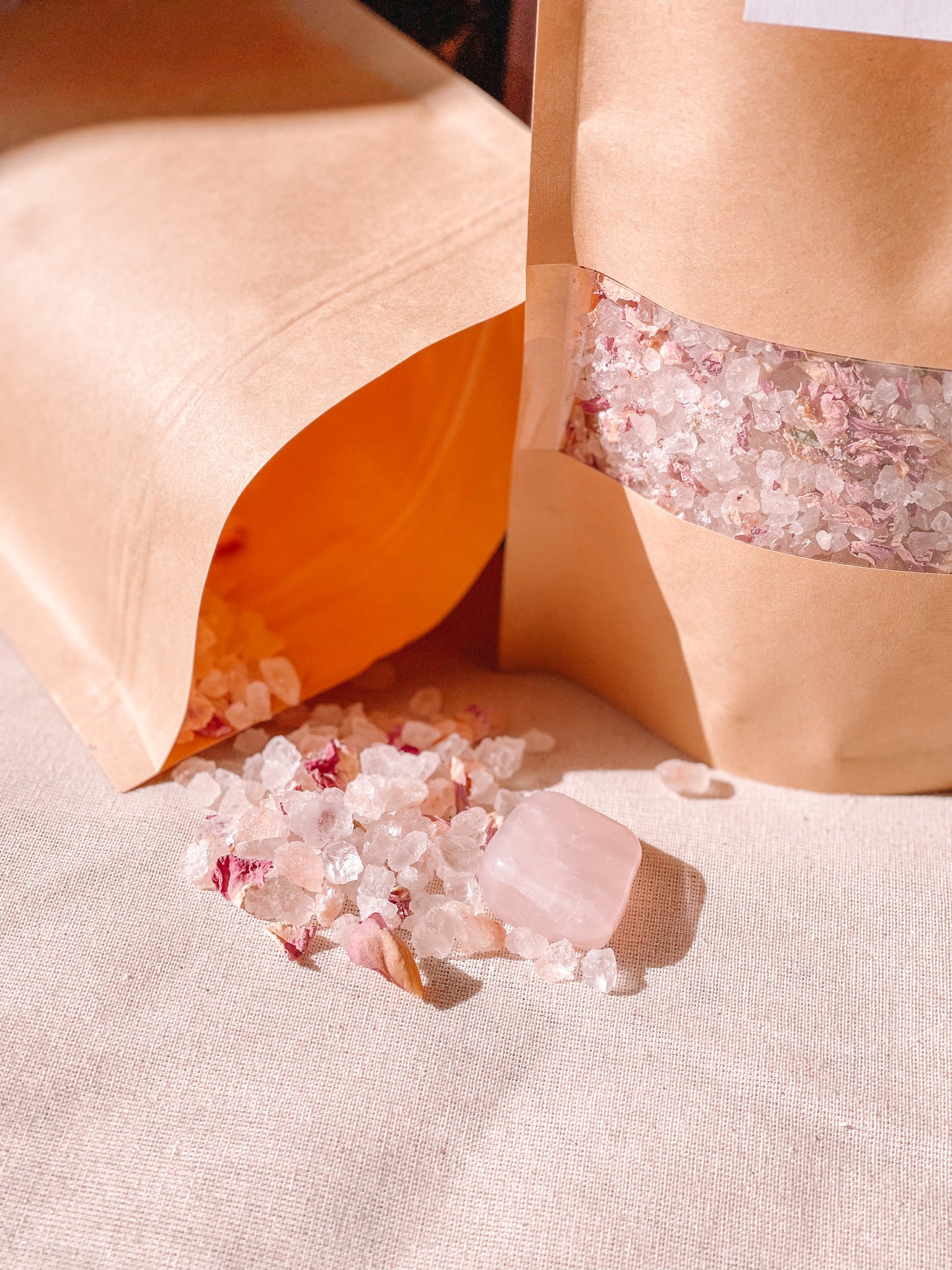 Een bruine papieren zak gevuld met badkristallen. Er ligt een andere papieren zak plat, met verspreide badkristallen.