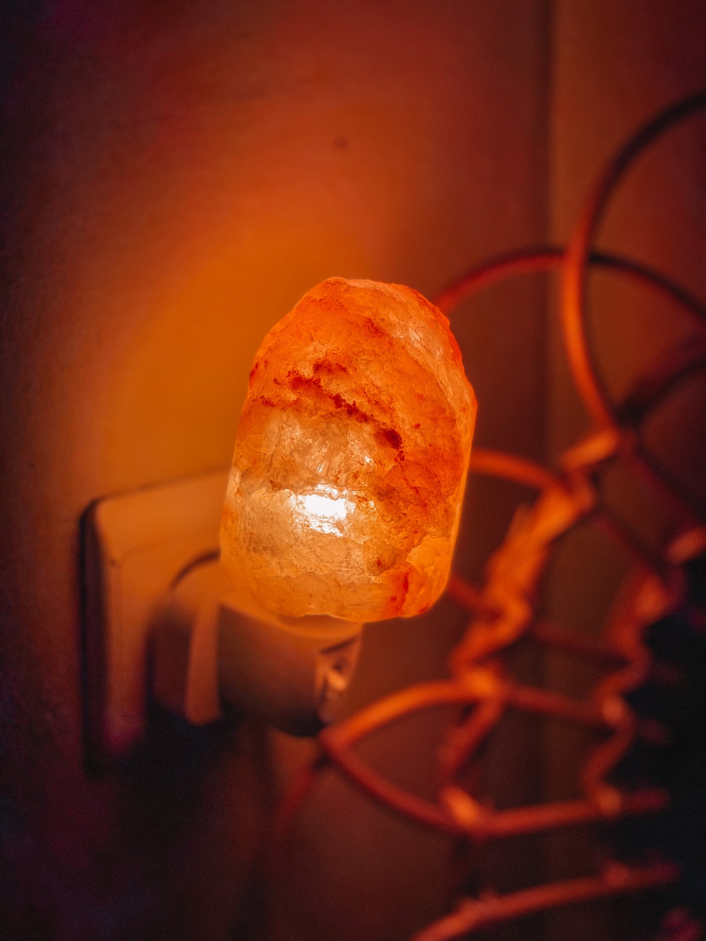 Een Himalaya zoutsteen nachtlampje in de vorm van een rots, aangesloten op een stopcontact en stralend met een warme, oranje gloed