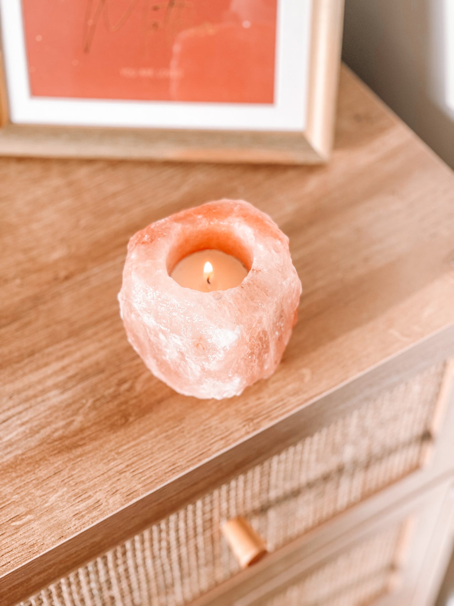 Een Himalaya zout theelichthouder met een brandend kaarsje erin. De theelichthouder staat op een houten oppervlak en op de achtergrond is een ingelijste foto te zien.