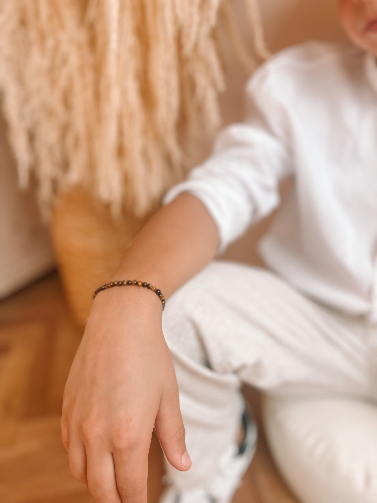 Jongen, wiens hand leunt op de knie, met rond de pols een edelsteen armbandje.