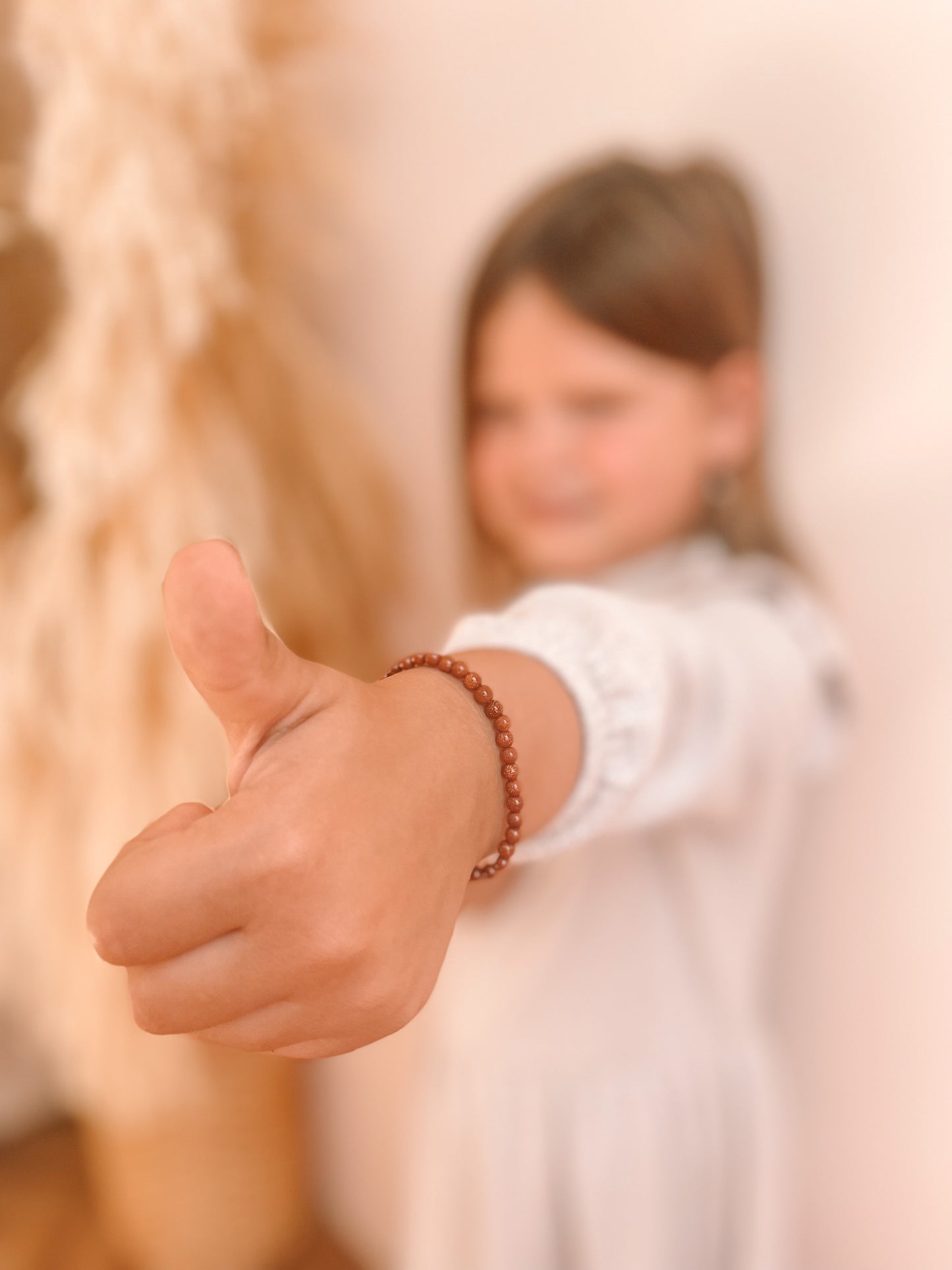 Meisje die haar duim omhoog steekt, de focus van de afbeelding ligt op de hand, waar rond de pols een edelsteen armbandje zit.