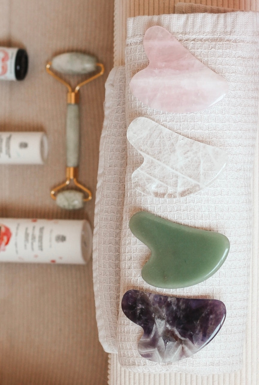 4 soorten Gua Sha op een handdoekje, met er rond skincare producten. 