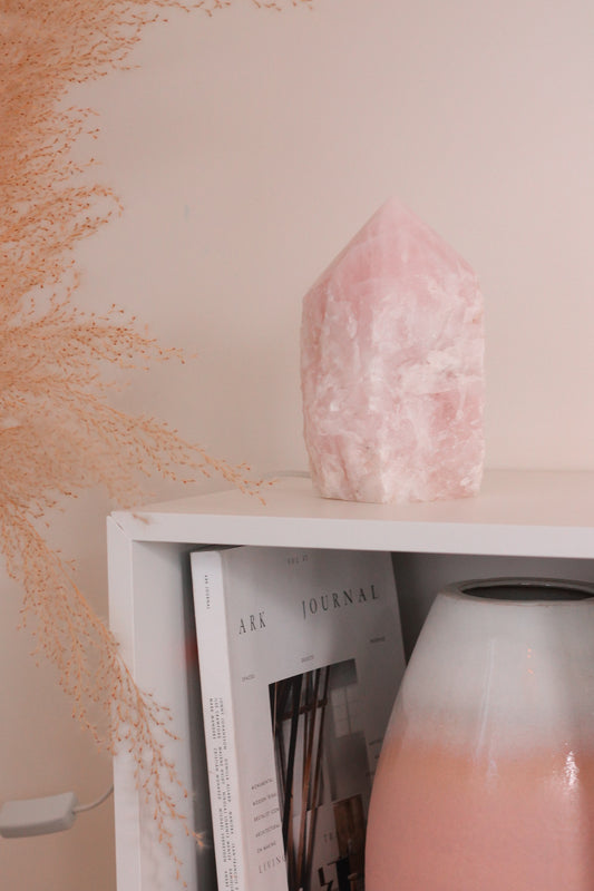 Rozenkwarts punt lamp op een witte kast. In de kast staat een boek en een grote vaas met witte en roze kleuren.