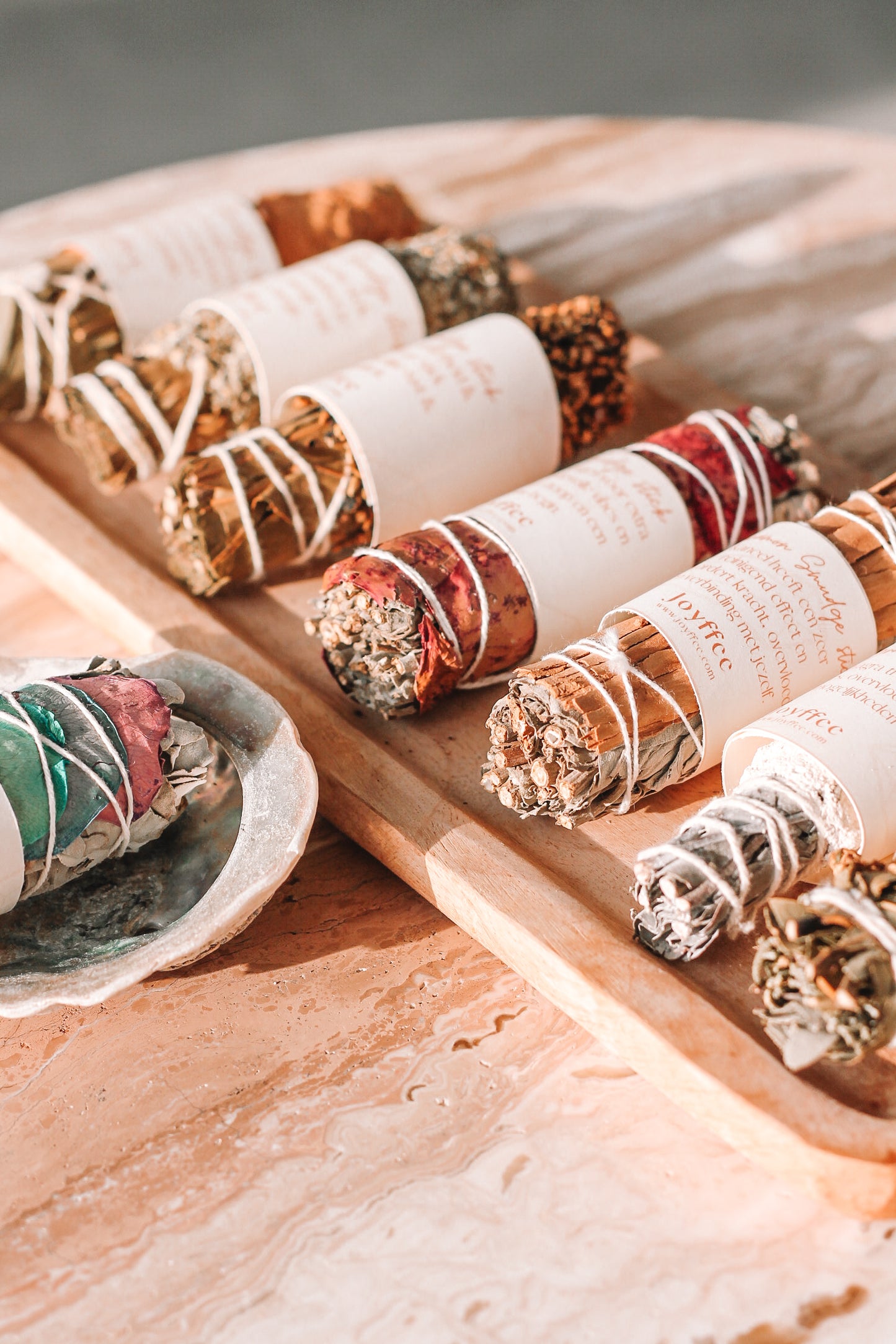 Een houten dienblad met verschillende smudge sticks, elk omwikkeld met wit touw en voorzien van een papieren label. De smudge sticks bestaan uit diverse kruiden en planten.