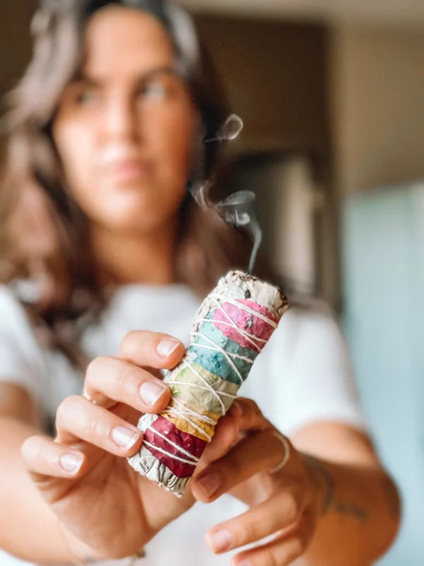 Een persoon houdt een aangestoken kleurrijke smudge stick vast met gekleurde rozenblaadjes.