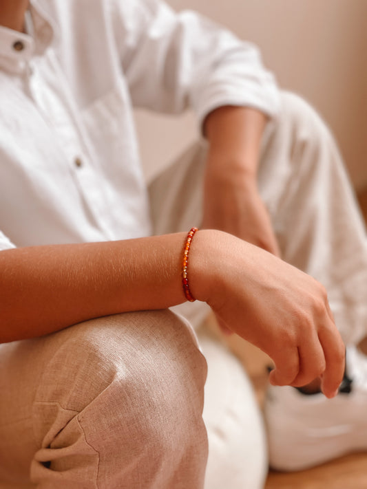 Jongen die zijn hand leunt op de knie, met rond de pols een Edelsteen armbandje. 
